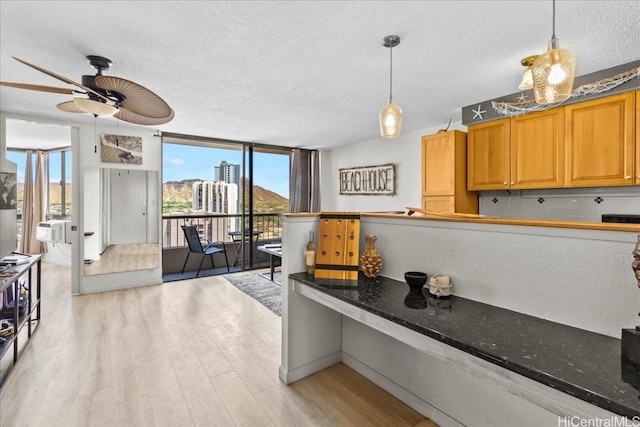 kitchen featuring dark stone countertops, hanging light fixtures, light wood-type flooring, and a wealth of natural light