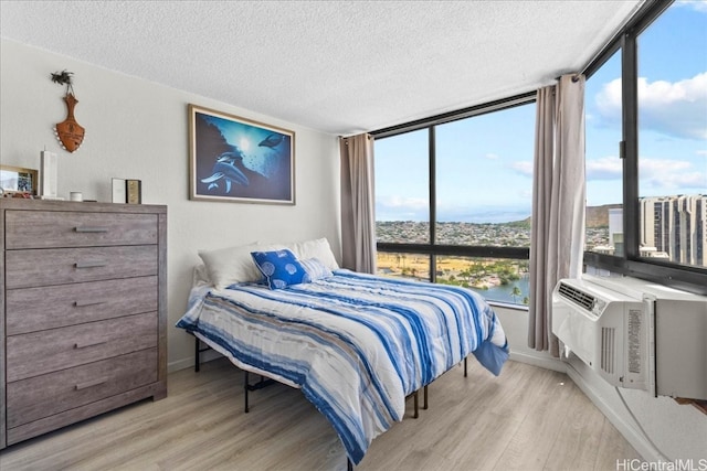 bedroom featuring a water view, light hardwood / wood-style floors, a textured ceiling, and floor to ceiling windows