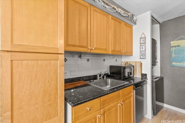 kitchen with appliances with stainless steel finishes, a textured ceiling, light wood-type flooring, dark stone countertops, and sink