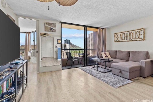 living room featuring ceiling fan, a textured ceiling, light wood-type flooring, and floor to ceiling windows