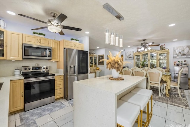 kitchen with a breakfast bar area, decorative light fixtures, a center island, light brown cabinets, and stainless steel appliances