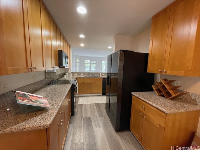 kitchen with kitchen peninsula, sink, black appliances, light stone countertops, and light wood-type flooring