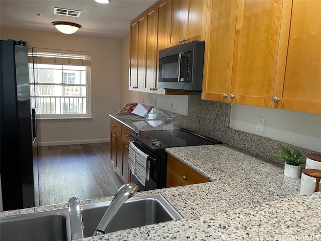 kitchen with hardwood / wood-style floors, tasteful backsplash, light stone counters, sink, and stainless steel appliances