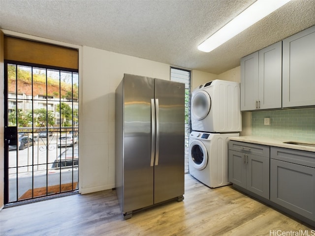 laundry area featuring stacked washer / drying machine, a textured ceiling, light hardwood / wood-style floors, and cabinets