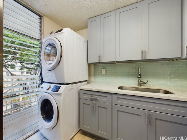 laundry area featuring cabinets, a healthy amount of sunlight, stacked washer / drying machine, and sink