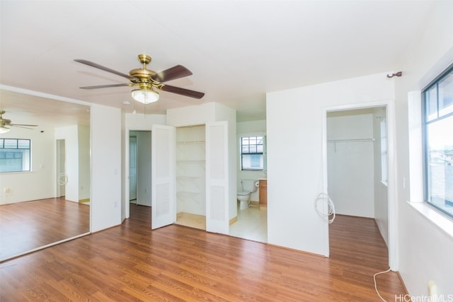 unfurnished bedroom with multiple windows, ensuite bathroom, hardwood / wood-style flooring, and ceiling fan