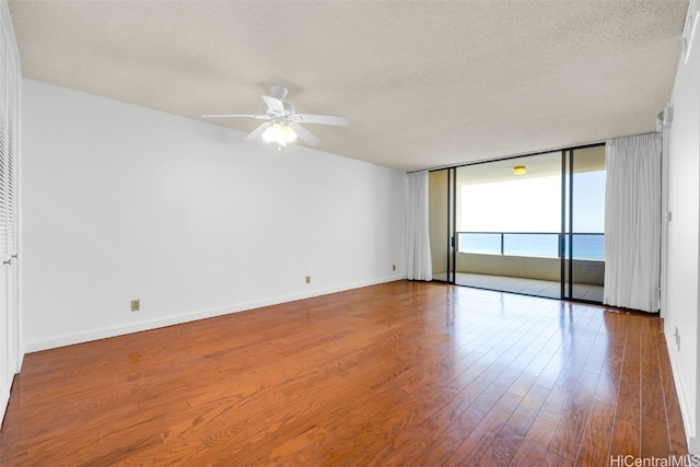 unfurnished room with ceiling fan, a textured ceiling, hardwood / wood-style flooring, floor to ceiling windows, and a water view