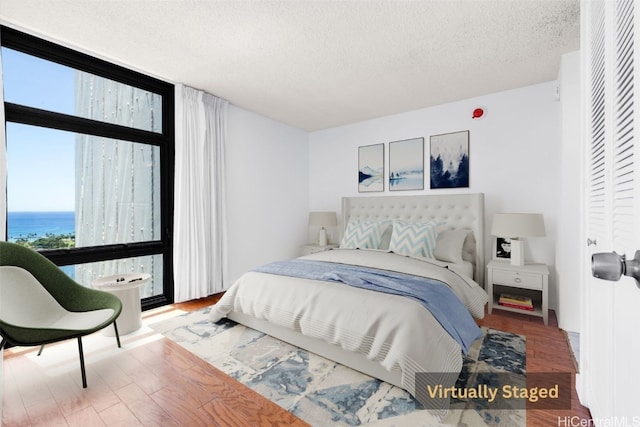 bedroom featuring a water view, hardwood / wood-style flooring, and a textured ceiling