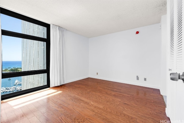 spare room featuring a water view, hardwood / wood-style flooring, and a textured ceiling