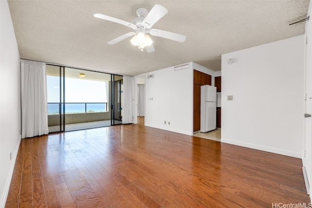 spare room featuring a water view, light wood-type flooring, expansive windows, a textured ceiling, and ceiling fan