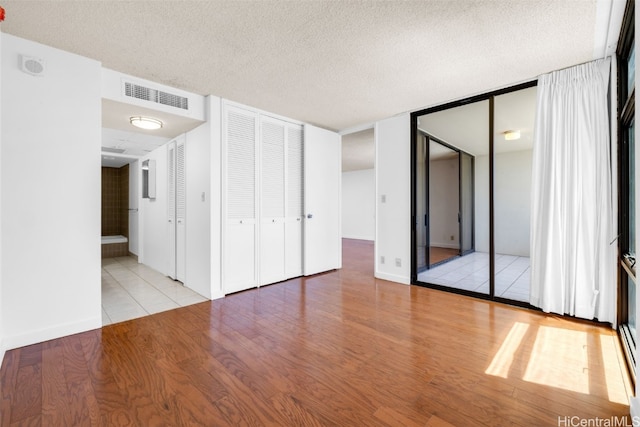 unfurnished bedroom with connected bathroom, a textured ceiling, and light hardwood / wood-style floors