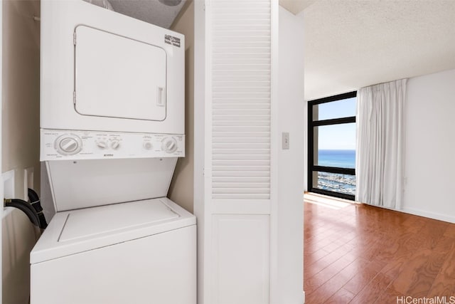 laundry area featuring stacked washing maching and dryer, a textured ceiling, wood-type flooring, and a water view