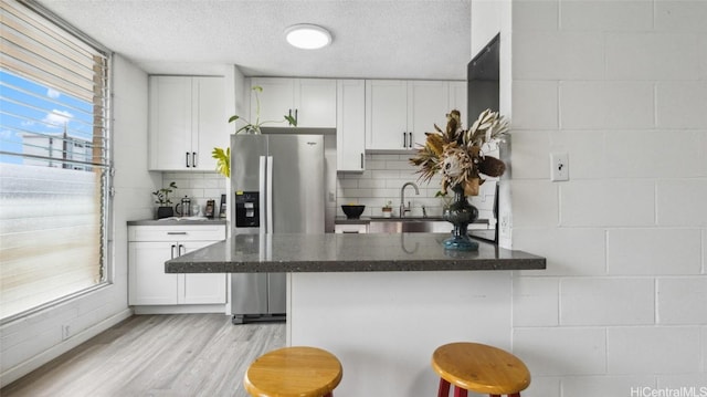 kitchen with a textured ceiling, white cabinetry, decorative backsplash, stainless steel fridge with ice dispenser, and a breakfast bar