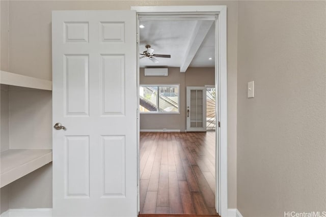 corridor featuring beamed ceiling, an AC wall unit, baseboards, and wood finished floors