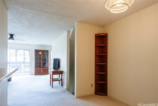 hall featuring a chandelier, a textured ceiling, and light colored carpet