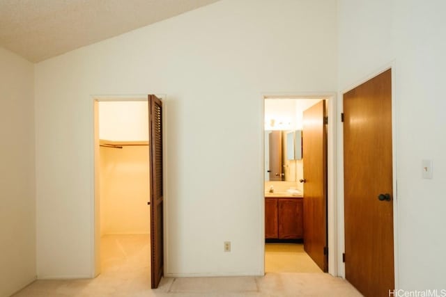 unfurnished bedroom featuring light carpet, ensuite bathroom, vaulted ceiling, a spacious closet, and a closet