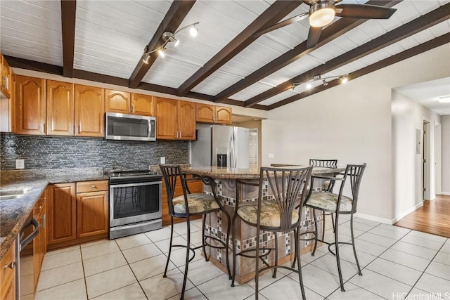 kitchen featuring light tile patterned floors, a kitchen bar, stainless steel appliances, and vaulted ceiling with beams