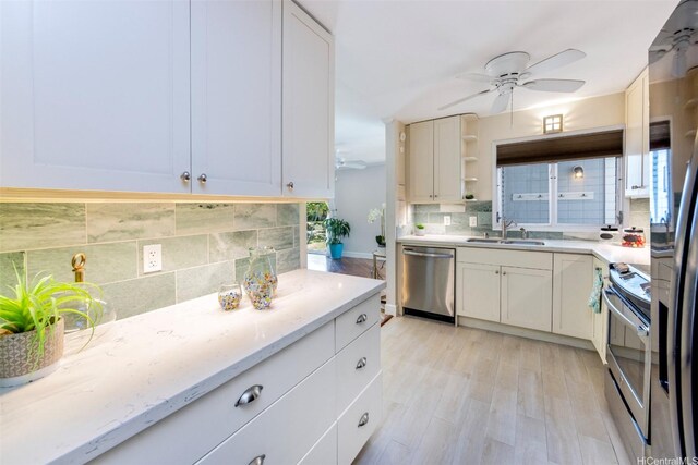 kitchen featuring a sink, light wood finished floors, stainless steel appliances, a ceiling fan, and backsplash