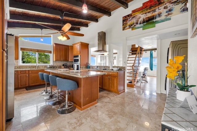 kitchen featuring wall chimney range hood, wood ceiling, a center island, stainless steel double oven, and beamed ceiling