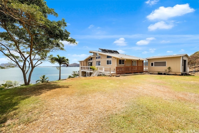 back of property with a deck with water view and a lawn