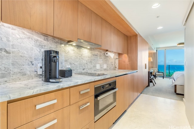 kitchen featuring oven, tasteful backsplash, exhaust hood, light stone countertops, and black electric cooktop