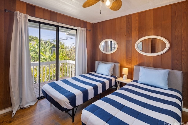 bedroom featuring access to exterior, wooden walls, ceiling fan, and dark hardwood / wood-style flooring