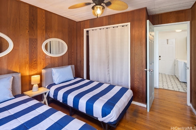 bedroom featuring washer and dryer, dark hardwood / wood-style flooring, wooden walls, and ceiling fan