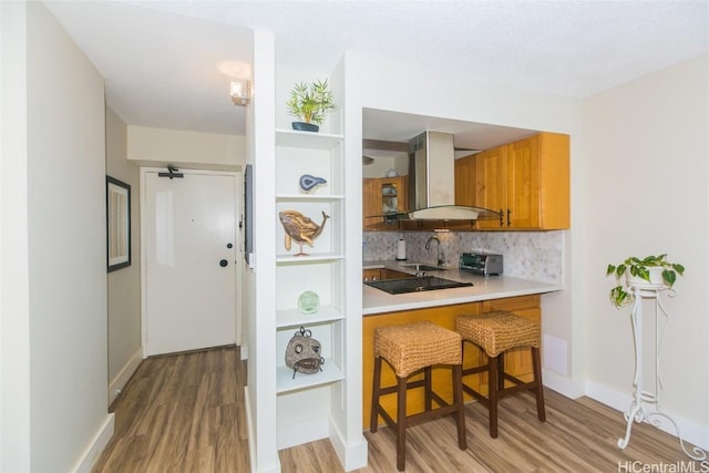 kitchen featuring sink, backsplash, a kitchen breakfast bar, island range hood, and light wood-type flooring