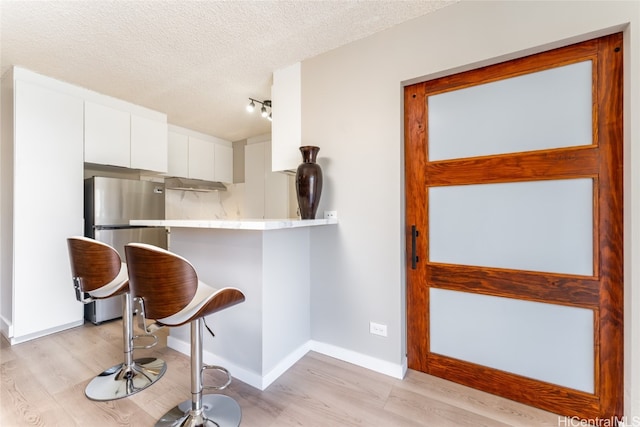 kitchen featuring a kitchen bar, white cabinetry, light hardwood / wood-style flooring, and stainless steel refrigerator