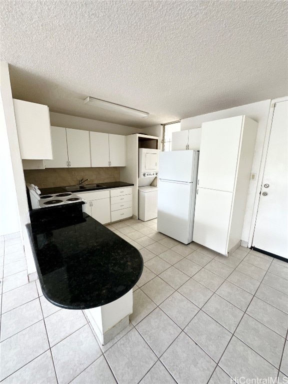 kitchen featuring white cabinetry, stacked washer / drying machine, a textured ceiling, and white appliances