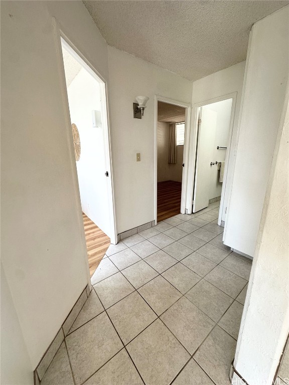 corridor featuring a textured ceiling and light tile patterned floors