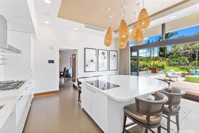 kitchen with wall chimney range hood, white cabinets, a kitchen island, stainless steel gas stovetop, and decorative light fixtures