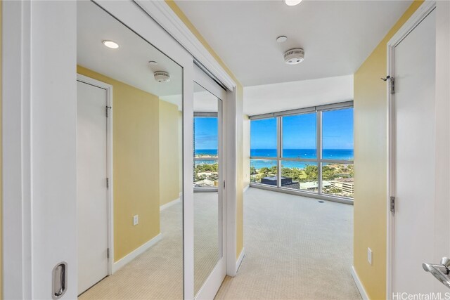 hall featuring expansive windows, light colored carpet, a water view, and a wealth of natural light