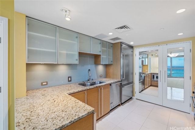 kitchen featuring french doors, kitchen peninsula, sink, appliances with stainless steel finishes, and light stone counters