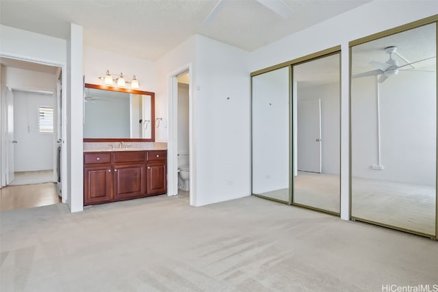 unfurnished bedroom featuring ensuite bathroom, sink, light colored carpet, and ceiling fan