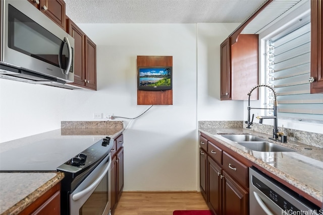 kitchen with light stone countertops, appliances with stainless steel finishes, sink, a textured ceiling, and light hardwood / wood-style floors