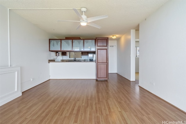 unfurnished living room with a textured ceiling, hardwood / wood-style flooring, sink, and ceiling fan