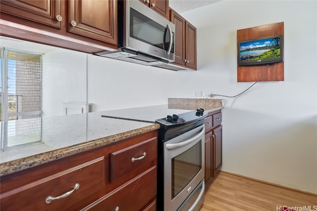 kitchen featuring stainless steel appliances, light stone countertops, and light wood-type flooring