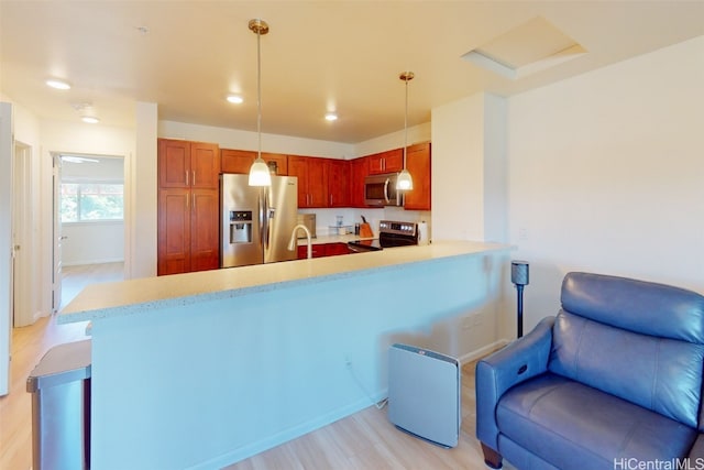 kitchen with kitchen peninsula, hanging light fixtures, appliances with stainless steel finishes, light wood-type flooring, and sink