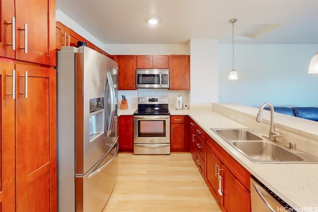 kitchen with hanging light fixtures, light hardwood / wood-style flooring, stainless steel appliances, sink, and light stone counters