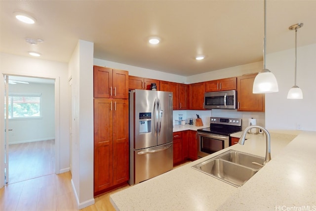 kitchen featuring hanging light fixtures, kitchen peninsula, sink, appliances with stainless steel finishes, and light stone counters