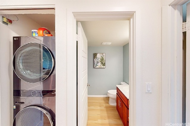 bathroom with vanity, stacked washing maching and dryer, wood-type flooring, and toilet