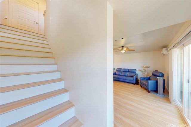 stairs with a wall mounted AC, wood-type flooring, and ceiling fan