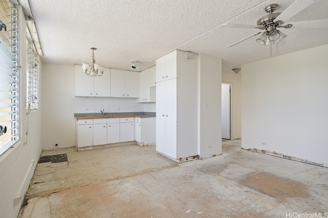 kitchen featuring a textured ceiling, decorative light fixtures, white cabinetry, and ceiling fan with notable chandelier