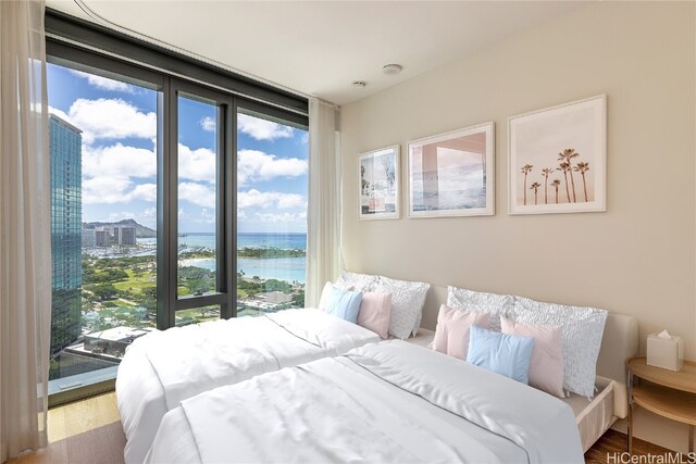 bedroom with floor to ceiling windows, a water view, and hardwood / wood-style flooring