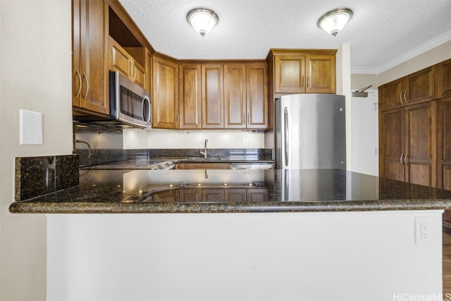 kitchen featuring appliances with stainless steel finishes, a textured ceiling, kitchen peninsula, dark stone countertops, and crown molding