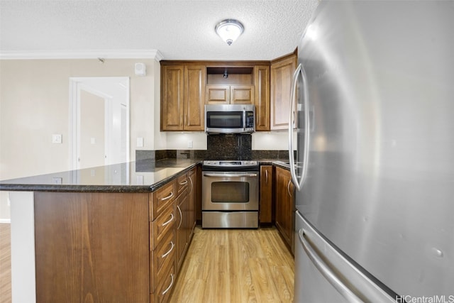 kitchen featuring appliances with stainless steel finishes, kitchen peninsula, light hardwood / wood-style floors, dark stone countertops, and ornamental molding