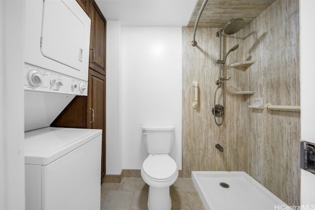 bathroom with a tile shower, stacked washer / dryer, toilet, and tile patterned flooring