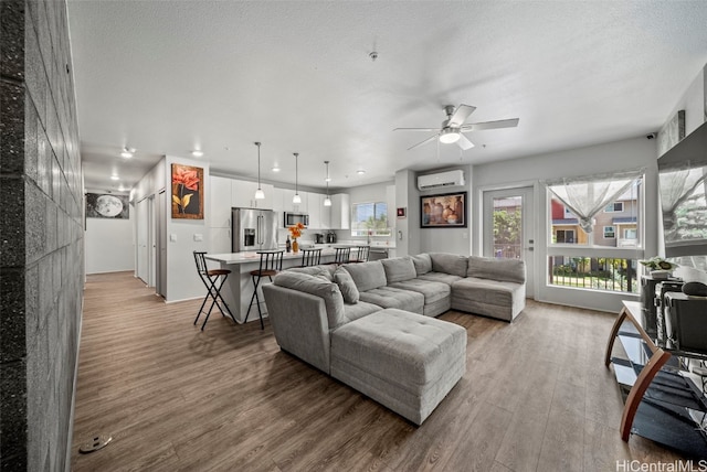 living room featuring a wall mounted AC, a textured ceiling, light hardwood / wood-style floors, and ceiling fan