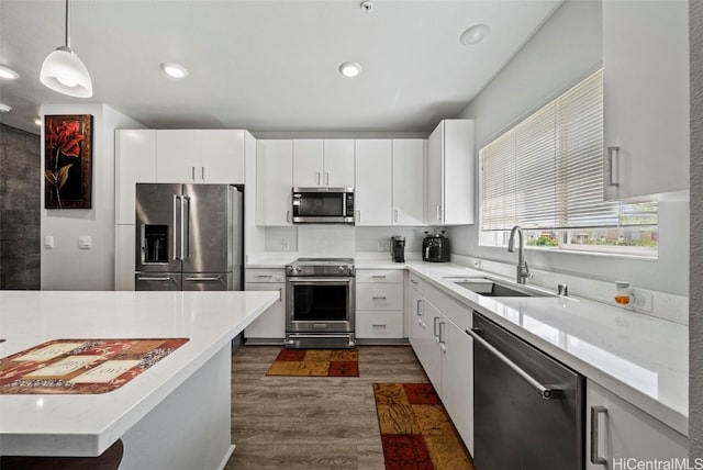 kitchen with hanging light fixtures, stainless steel appliances, sink, white cabinets, and dark hardwood / wood-style flooring